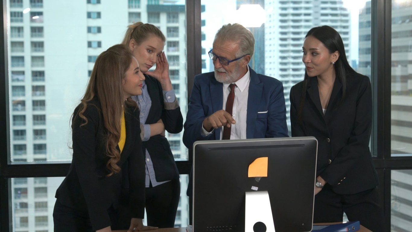 Four business professionals engaged in conversation around a computer in a modern office.