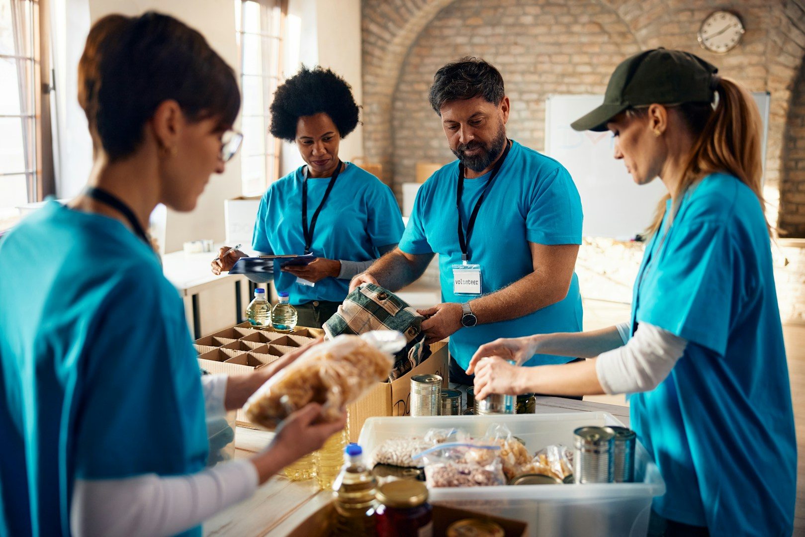 Four people in blue shirts volunteer together, preparing food in a community kitchen.
